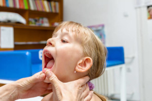 Little girl is having systematic examination with open mouth for checkup tonsils in doctor's office.