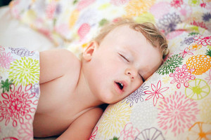 Cute little Caucasian boy with blond hair sleeping in a big bed on the pillow and covered with blanket. Little boy sleeping with his mouth open. Sweet dreams. Little boy in his parent's bed. Toddler a the big bed.